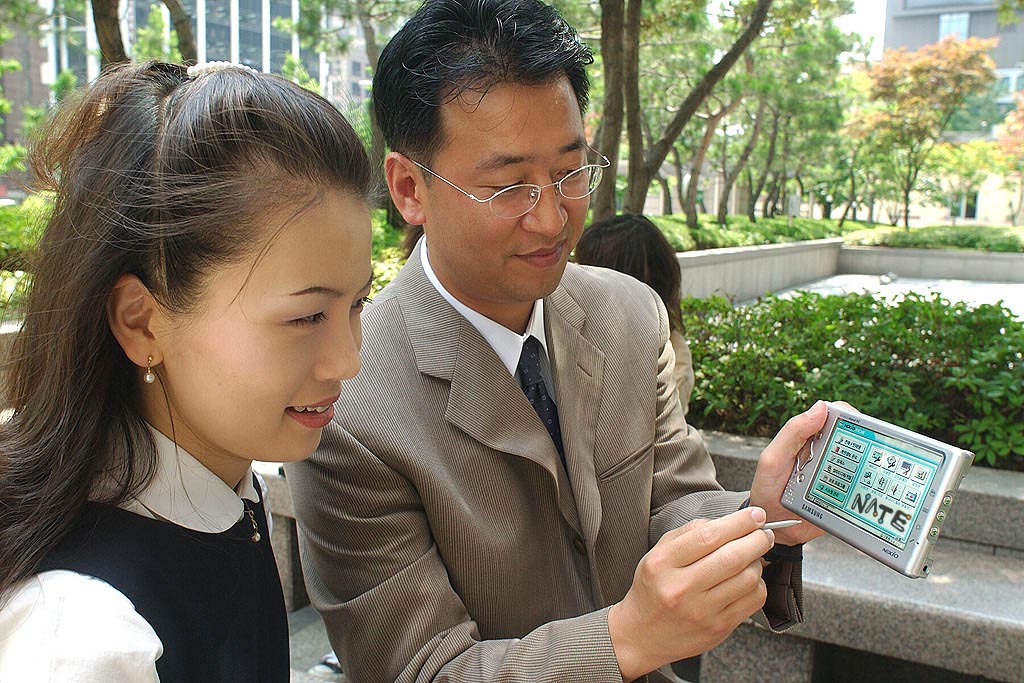 Photo shows an employee of an insurance company (male) explaining the insurance product package to an employee of SK Telecom (female) through the NATE SFA service.
